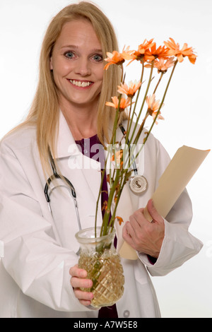 Lächelnde kaukasische Ärztin, die Blumen und einen Patientenordner in einem Gesundheitswesen hält, USA. Stockfoto