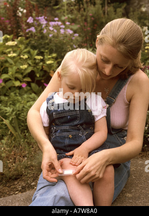 Mutter, die einen Gips auf eine Wunde eines Kleinkindes im Garten aufsetzt, Großbritannien Stockfoto