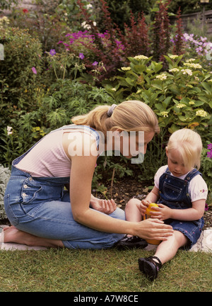 Mutter, die Sonnencreme auf ein Bein eines Kindes im Garten anwendet, Großbritannien Stockfoto