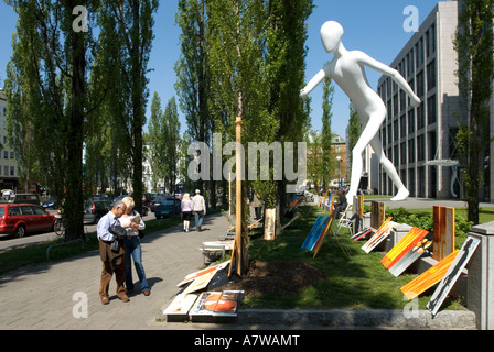 Mann und Frau, die einen Blick auf Kunstwerke Gemälde in der Leopoldstraße riesige Statue namens Walking Mann im Hintergrund München Bayern Stockfoto