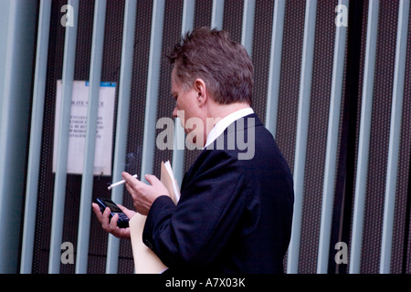 Raucher in Street in London während der Raucherpause Anzeigen von Nachrichten auf dem Handy Stockfoto