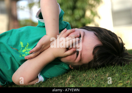 Verspielte junge (ca. 3-4 Jahre alt) Festlegung auf Rasen mit Händen bedeckte Gesicht Stockfoto