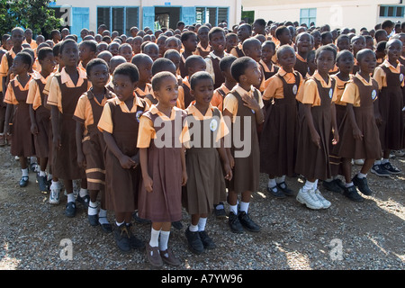 Gemischte Gruppe von Juniorkindern, hauptsächlich Mädchen in Uniform, bei Schulversammlung außerhalb von Klassenräumen vor Klassen in Ghana, Westafrika Stockfoto