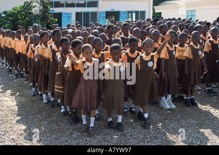 Gemischte Gruppe von Schulkindern, meist Junioren, marschieren vor Schulgebäuden in die Versammlung vor dem Unterricht in Ghana, Westafrika Stockfoto
