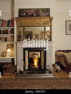 Kleines Gemälde und antike vergoldete Spiegel über Kamin mit Feuer im traditionellen Stadthaus Wohnzimmer beleuchtet Stockfoto