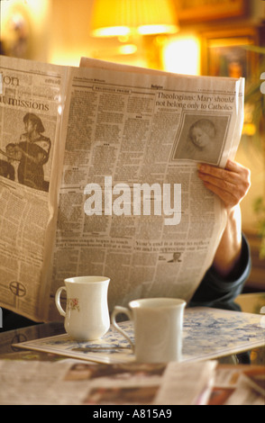 Pensionierte Frau beginnen Sie ihren Tag durch das Lesen eines Zeitung Religion Abschnitts und Kaffeetrinken am Küchentisch Stockfoto