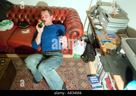 Junger Mann trinken Bier gelehnt ein rotes Leder-Sofa in einem Raum mit Büchern, CDs und Musik-system Stockfoto