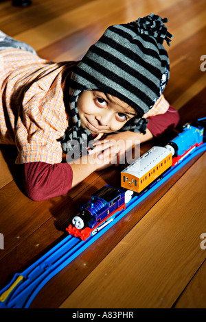 Junge im Alter von 5 Jahren trägt Hut und Lügen auf polierten Holzboden in Sonne mit Spielzeug Zug set Stockfoto