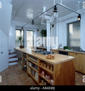 Offene Regale in hölzernen Insel Einheit unter röhrenförmige Beleuchtung Spur in modernen weißen Loft Umbau Küche Stockfoto