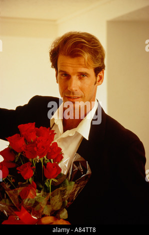 Indoor Porträt junger Mann, Blumenstrauß aus roten Rosen. Stockfoto