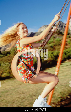 Junge Frau im Sommerkleid auf Schaukelsitz in Park Spielplatz. Stockfoto