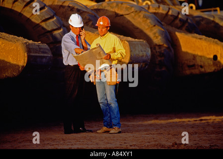 Zwei Männer stehen im Freien durch riesige Erde bewegenden Maschine an Straßenbaustelle. Stockfoto