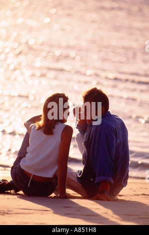Im freien Rückseite des jungen romantisches Paar Mann und Frau sitzen am Strand bei Sonnenuntergang. Stockfoto
