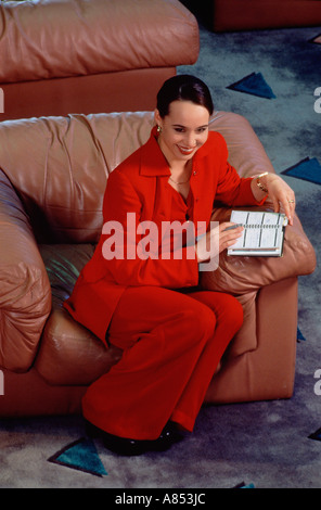 Hohe Sicht der jungen Frau in roten Hosenanzug in Ledersessel sitzend. Stockfoto