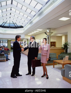 Zwei Männer Gruß Händedruck und eine Frau im Empfang Atrium des modernen Gebäudes. Stockfoto