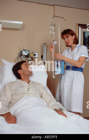 Mittleren Alter Mann im Krankenhaus mit Krankenschwester am Krankenbett eine Kochsalzlösung Infusion anpassen. Stockfoto