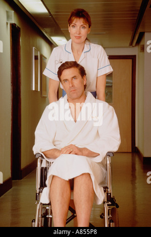 Weibliche Krankenschwester männliche Patienten im Rollstuhl Korridor entlang schieben. Stockfoto