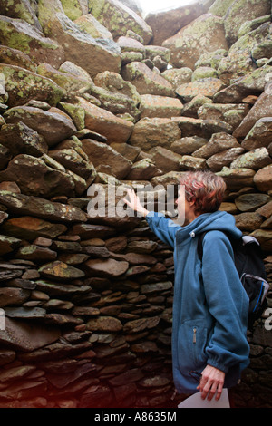 junge Frau in einer Hütte in Form einer Bienenwabe, gebaut aus Steinen auf der Dingle-Halbinsel an der westlichen Küste von Irland Stockfoto