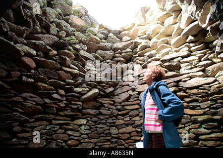 junge Frau in einer Hütte in Form einer Bienenwabe, gebaut aus Steinen auf der Dingle-Halbinsel an der westlichen Küste von Irland Stockfoto