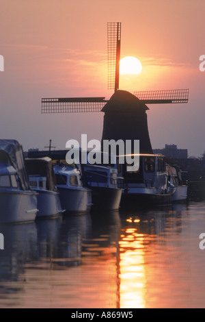 Boote vertäut am Kanal in der Nähe von Alkmaar mit Sonnenuntergang hinter der Windmühle in Holland Stockfoto