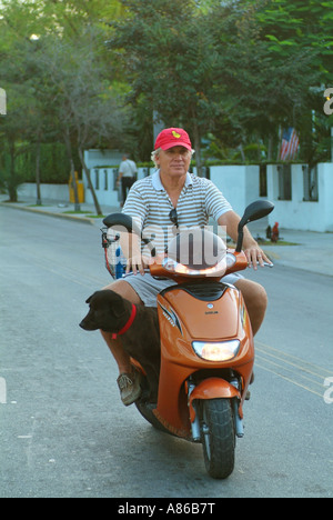 Ein Mann reitet auf seinem Roller auf der Straße mit einem schwarzen Hund zu seinen Füßen Stockfoto