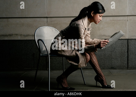 Junge asiatische Frau sitzt auf einem Stuhl, eine Zeitung lesen Stockfoto