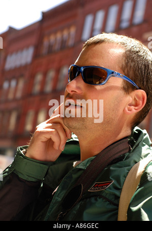 Junger Mann mit blauen Fassungen und Sonnenbrillen, die reden auf seinem Handy Mobilfunk Stockfoto