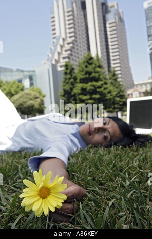 Eine Frau liegt auf dem Rasen mit einer Blume in der Hand. Stockfoto