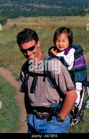 Vater trägt Adoptivtochter junge Amerikaner asiatischer Abstammung auf seinem Rücken in Rucksack Stockfoto