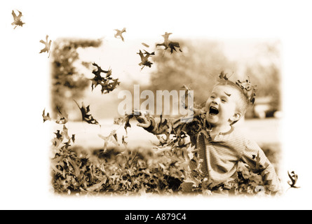 Kleiner Junge spielt in einem Haufen von Rake Blätter wie er lassen in die Luft und lacht wirft Stockfoto