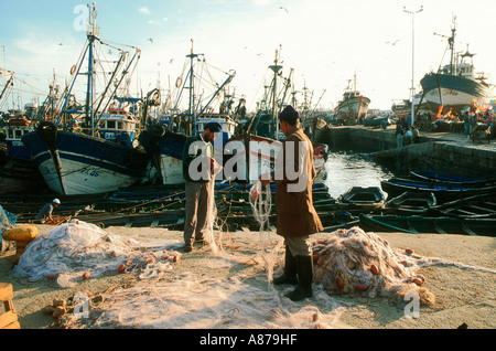 Fischer reparieren Netze im Hafen mit Fischerbooten im Hintergrund. Essaouira, Marokko Stockfoto