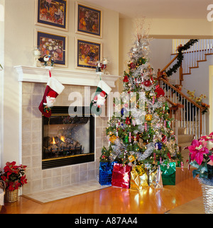 Dekorierten Weihnachtsbaum umgeben mit bunt verpackte Geschenke neben einem Kamin mit zwei Weihnachtsstrümpfe aufgehängt Stockfoto