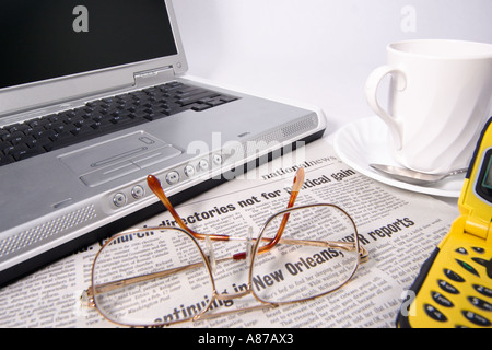 Offener Laptop-Notebook-Computer mit Zeitungsaugengläsern Kaffeetasse auf Untertasse und gelbem Handy auf weißem Hintergrund Stockfoto