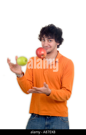 Junger Mann in seinen späten Teenager, lässig gekleidet, spielen mit zwei Äpfeln und lächelt in die Kamera. Stockfoto