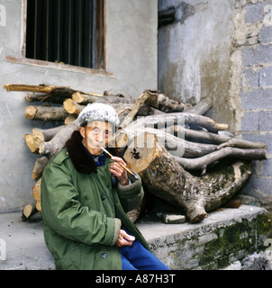 Ältere lokale Mann mit langen grünen Armeemantel sitzt, raucht seine Pfeife auf der Straße, Yangshuo, Provinz Guangxi, China Stockfoto