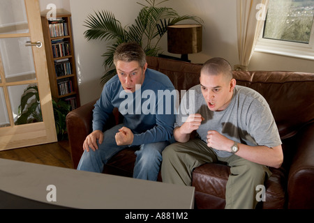 -Modell veröffentlicht. Zwei Fußball-Fans auf Sofa vor dem Fernseher, schreien und Spott. Stockfoto