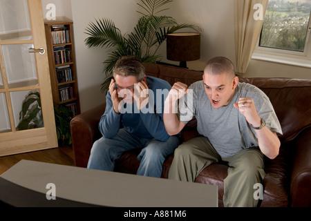 -Modell veröffentlicht. Zwei Fußball-Fans auf Sofa vor dem Fernseher, schreien und Spott. Stockfoto