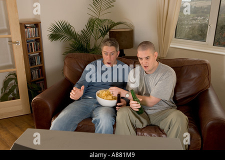 -Modell veröffentlicht. Zwei Fußball-Fans auf Sofa vor dem Fernseher sitzen, schreien und Spott während Chips essen und trinken Bier. Stockfoto