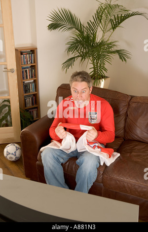 -Modell veröffentlicht. England Fußball-Fan sitzt zu Hause auf Sofa beobachten Match im Fernsehen aufgeregt und glücklich als Team gewinnt. Stockfoto