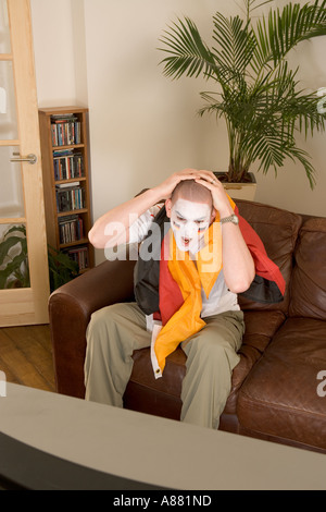 -Modell veröffentlicht. Deutsche Fußball-Fan sitzt auf dem Sofa vor dem Fernseher suchen aufgeregt, als Team gerade verloren hat. Stockfoto