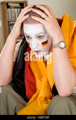 -Modell veröffentlicht. Deutsche Fußball-Fan sitzt auf dem Sofa vor dem Fernseher suchen aufgeregt, als Team gerade verloren hat. Stockfoto