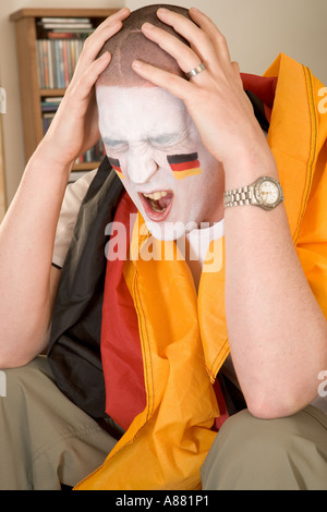 -Modell veröffentlicht. Deutsche Fußball-Fan sitzt auf dem Sofa vor dem Fernseher suchen aufgeregt, als Team gerade verloren hat. Stockfoto