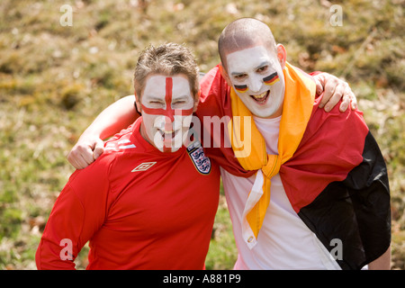 England und deutsche Fußballfans umarmen einander in guter Geist, glücklich lächelnde Gesichter mit Nationalfarben bemalt. Stockfoto