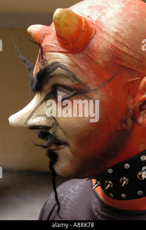 Seitenprofil eines männlichen gehörnten Teufels mit großer Nase, roter Gesichtsfarbe, prothetischen Hörnern, buschigen Augenbrauen und schwarzem Stachelkragen. Stockfoto