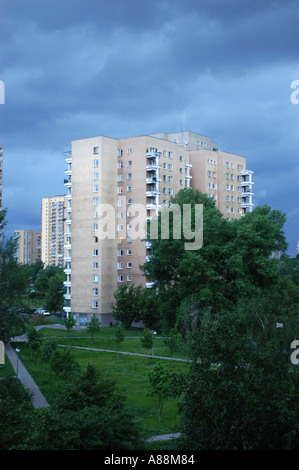 Beton-Wohnblock Warschau, Polen. Hohes Wohngebäude umgeben von grünen Bäumen und Parklandschaft unter einem dramatisch stürmischen blauen Himmel. Stockfoto