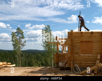 Älterer Mann, der eine Blockhütte baut und oben auf der Kabinenwand steht und eine neue Balk darauf installiert, Finnland Stockfoto