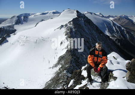 Bergsteiger sitzt auf den Felsen vor einem schneebedeckten Berg Kharkhiraa mongolischen Altai in der Nähe von Ulaangom Uvs Aymag Mongolei Stockfoto