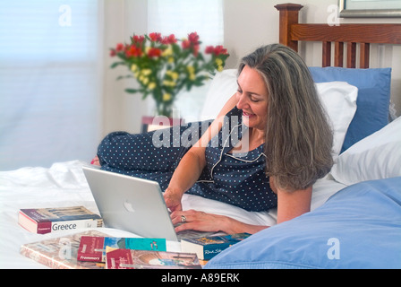 Blick auf Jugendliche Reife Frau mit langen grauen Haaren auf ihrem Laptop arbeiten, während Sie gemütlich im Bett Stockfoto