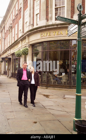 Ein Paar, das Arm in Arm mit dem Bettys Cafe und den Teestuben draußen läuft. York Großbritannien Stockfoto