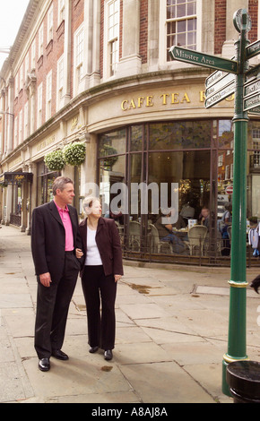 Ein Paar, das Arm in Arm mit dem Bettys Cafe und den Teestuben draußen läuft. York Großbritannien Stockfoto